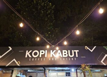 Pengunjung sedang menikmati kopi dengan latar belakang kabut dan pegunungan di Kopi Kabut Sevillage.